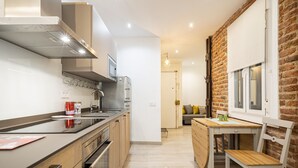A modern kitchen with stainless steel appliances, a wooden dining table, and a brick wall. - COZY APARTMENT IN THE NEIGHBORHOOD OF SALAMANCA JOG48 (Madrid)