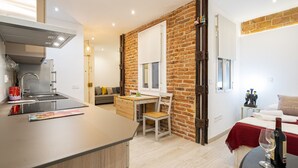 A modern kitchen with a built-in stove, a dining area with a wooden table and chairs, a brick accent wall, and a cozy bedroom with a bed and a nightstand. - COZY APARTMENT IN THE NEIGHBORHOOD OF SALAMANCA JOG48 (Madrid)