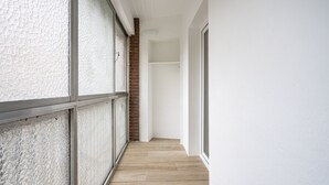 A narrow corridor with a wooden floor, white walls, and a glass door on the left.