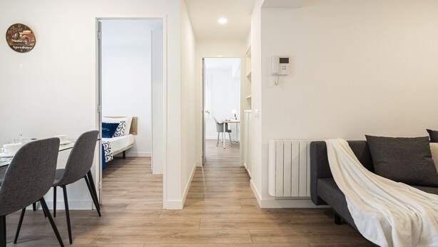 A modern apartment with a dining area, a sofa, and a hallway leading to a kitchen.