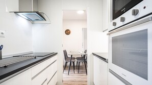 A modern kitchen with white cabinetry, a built-in oven, and a dining area with a table and chairs.