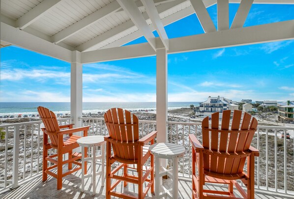 A covered outdoor seating area with three wooden chairs and a table, overlooking a beach and ocean. - Gulf front home w/6 seater golf cart, priv. pool, direct beach access (Santa Rosa Beach)