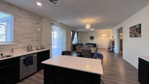 A modern kitchen with a marble backsplash, a central island, and a dining area with a round table and chairs. - Cozy and Comfy Stay at a Bargain! (Woodland)