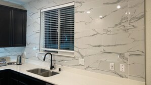 A kitchen with marble backsplash, a window with blinds, a sink, and a toaster. - Cozy and Comfy Stay at a Bargain! (Woodland)