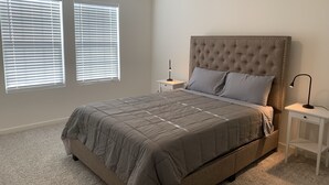 A bedroom with a large bed, two bedside tables, and two windows with blinds. - Cozy and Comfy Stay at a Bargain! (Woodland)