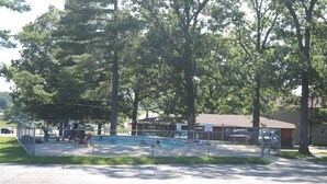Piscina pública com área cercada, rodeada por árvores e um edifício ao fundo.