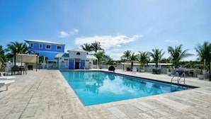 A swimming pool with a tiled deck, palm trees, and a blue building in the background. - Tropical Key Largo RV Getaway with Boat Ramp & Golf Cart (Key Largo)