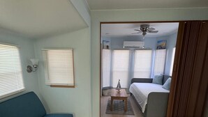 A living room with a blue sofa, a small table, and a bed with a grey headboard. - Tropical Key Largo RV Getaway with Boat Ramp & Golf Cart (Key Largo)