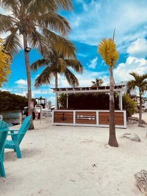 A beachside bar with a wooden structure, chairs, and palm trees. - Tropical Key Largo RV Getaway with Boat Ramp & Golf Cart (Key Largo)