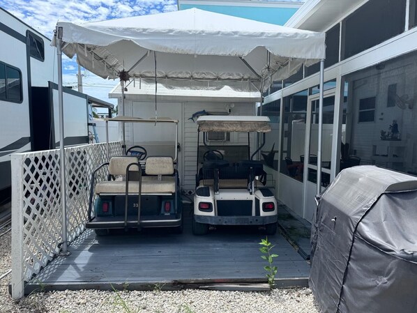 A covered outdoor seating area with two golf carts, a white fence, and a covered grill. - Tropical Key Largo RV Getaway with Boat Ramp & Golf Cart (Key Largo)
