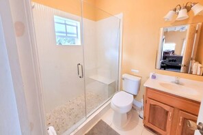 A bathroom with a glass shower enclosure, a toilet, a sink with a mirror, and a tiled floor.