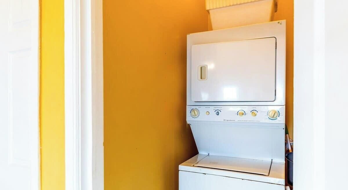 A white laundry machine in a room with yellow walls.