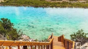 A wooden walkway leading to a body of water with clear turquoise water and a view of the coastline.