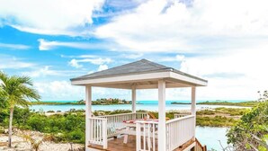 Ein Pavillon mit Holzterrasse und weißen Geländern mit Blick auf einen Strand und das Meer.