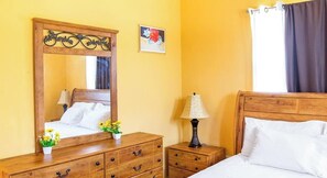 Une chambre d’hôtel avec un lit en bois, une table de chevet avec une lampe, une commode et un miroir.