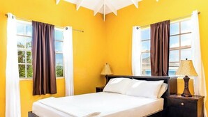Une chambre avec un lit, deux tables de chevet avec des lampes et des rideaux aux fenêtres.
