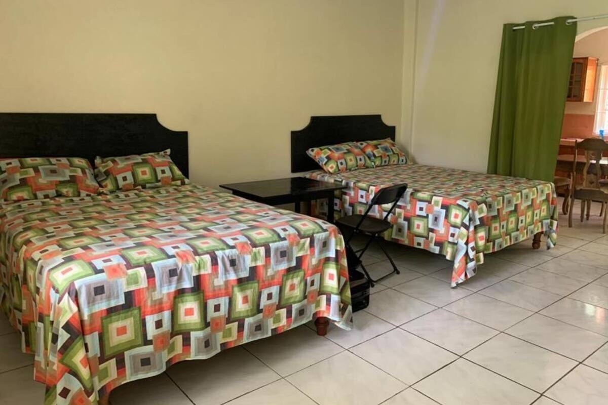 A hotel room with two beds, each with a colorful quilt, a small table, and a green curtain.