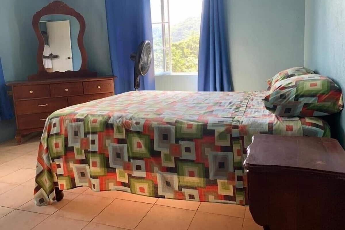 A bedroom with a bed, a dresser, a mirror, and a window with curtains.