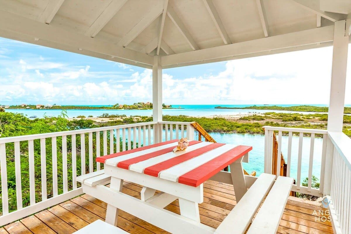 Un espace extérieur abrité doté d’une terrasse en bois, de rampes blanches et d’une table à rayures rouges et blanches.