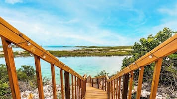 A wooden staircase leading to a beach with clear turquoise water and a view of the horizon.