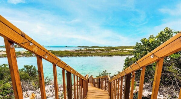 Una escalera de madera que lleva a una playa con agua turquesa cristalina y vistas al horizonte.