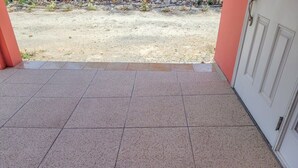 A tiled patio area with a view of a gravel path and a building in the background. - Chalk Sound Lagoon Cottage with Kayak Dock (Providenciales)