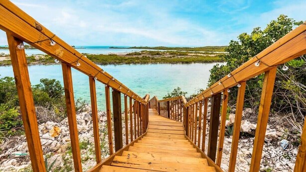 A wooden staircase leading to a coastal area with clear water and greenery. - Chalk Sound Lagoon Cottage with Kayak Dock (Providenciales)