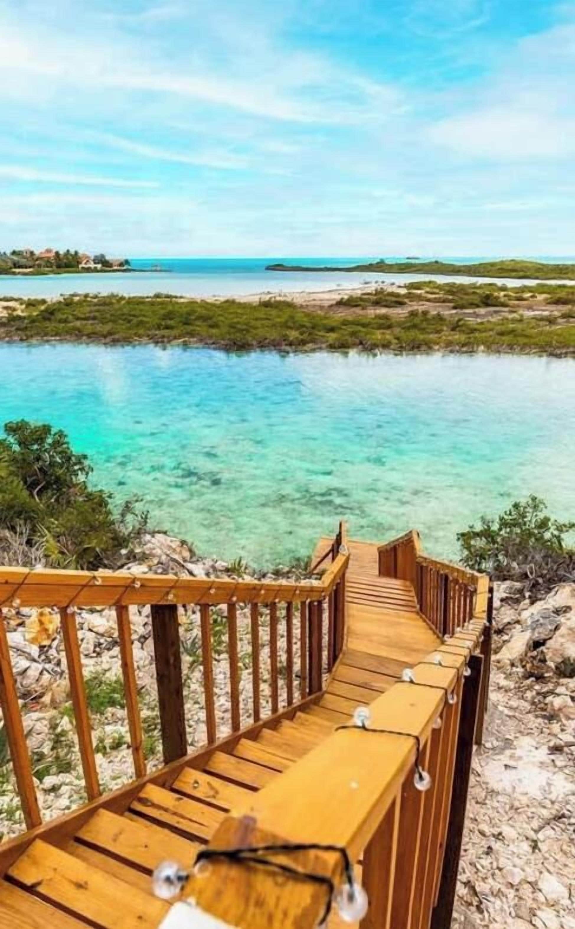 A wooden walkway leading to a body of water with clear turquoise water and a view of the coastline.