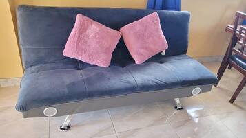 A dark blue sofa with two pink cushions, a wooden chair, and a tiled floor.