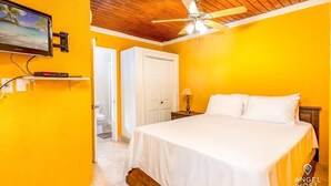 A bedroom with a bed, a ceiling fan, a television mounted on the wall, and a door leading to another room. - Chalk Sound Lagoon Cottage with Kayak Dock (Providenciales)