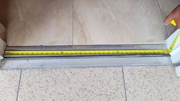 A measuring tape placed across a floor with a tiled surface and a carpeted area.