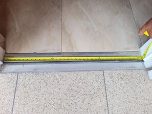 Una cinta métrica colocada sobre un suelo con baldosas y una zona alfombrada.