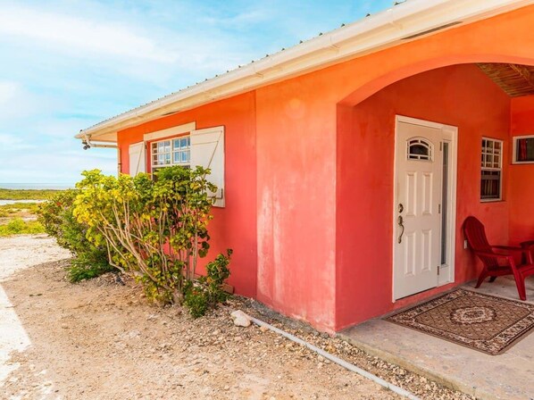 A red building with a white door, two windows, and a small porch with red chairs.