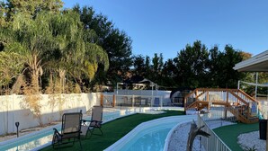 Ein Außenpool mit Holzterrasse, umgeben von einem weißen Zaun und Bäumen.