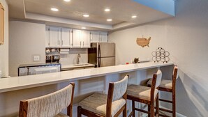 A modern kitchen with white cabinets, a stainless steel refrigerator, and a bar area with wooden chairs. - Mountainside Retreat - Sleeps 4 (Frisco)