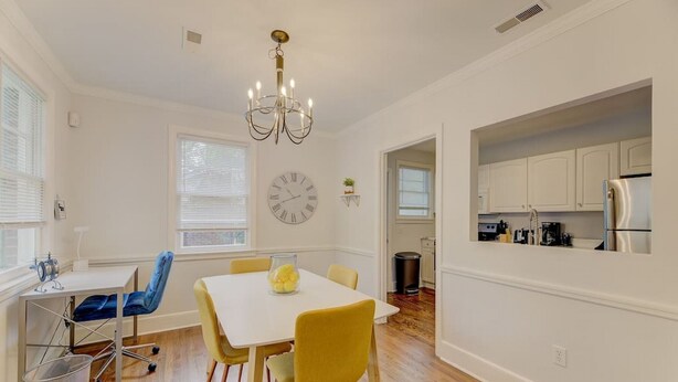 A dining area with a white table, yellow chairs, a chandelier, and a clock on the wall. - Charming Earlewood Cottage - Minutes from Downtown (Columbia)