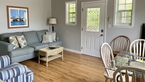 A living room with a grey sofa, a coffee table, a dining table with chairs, a ceiling fan, and a door with a window.