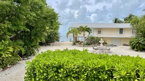 A two-story building with a balcony, surrounded by lush greenery and a sandy beach.