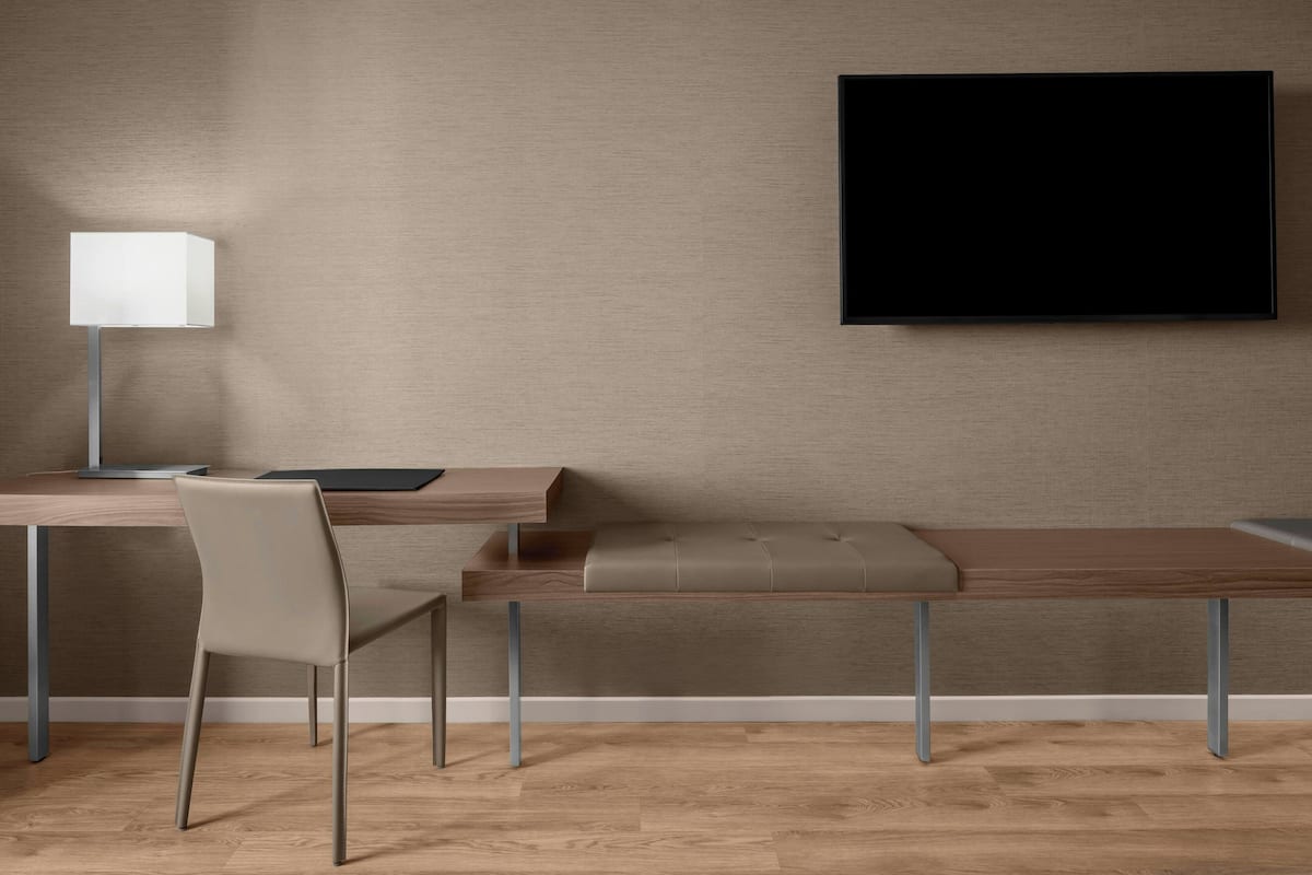 A modern room with a desk, chair, bench, and a flat-screen TV mounted on the wall.