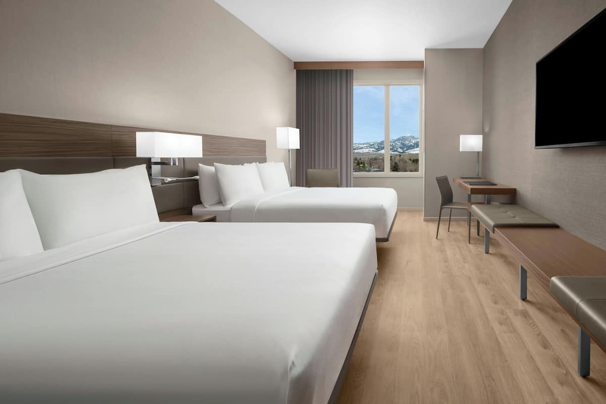 A hotel room with two beds, a desk, a chair, and a TV.