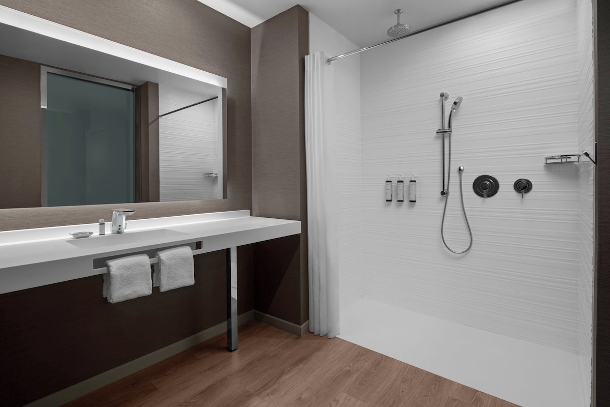 A modern bathroom with a large mirror, a white sink, a shower with a glass door, and a towel rack.