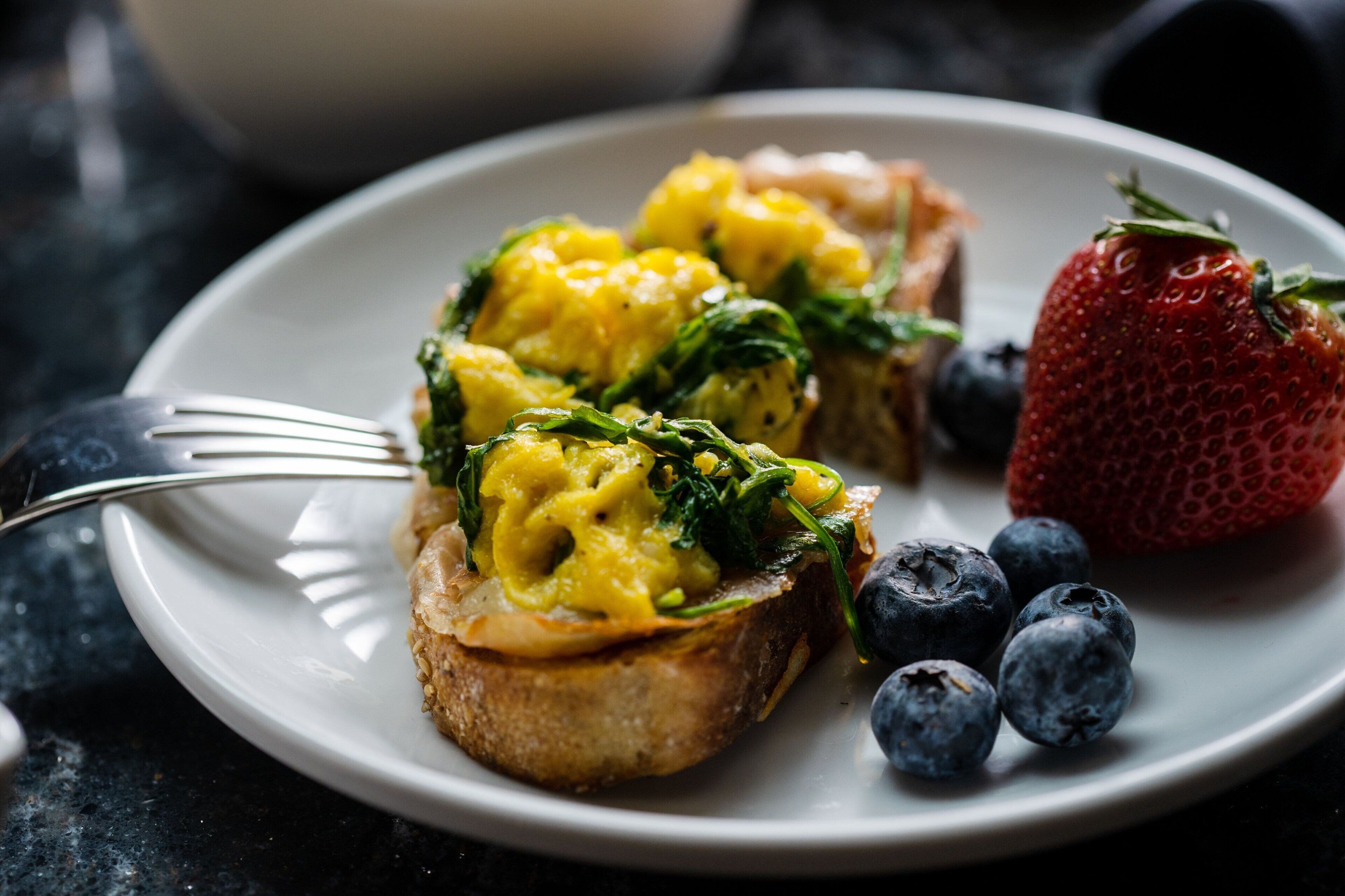 A plate with scrambled eggs, spinach, and a strawberry.