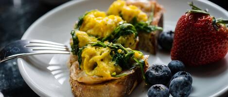 A plate with scrambled eggs, spinach, and a strawberry.