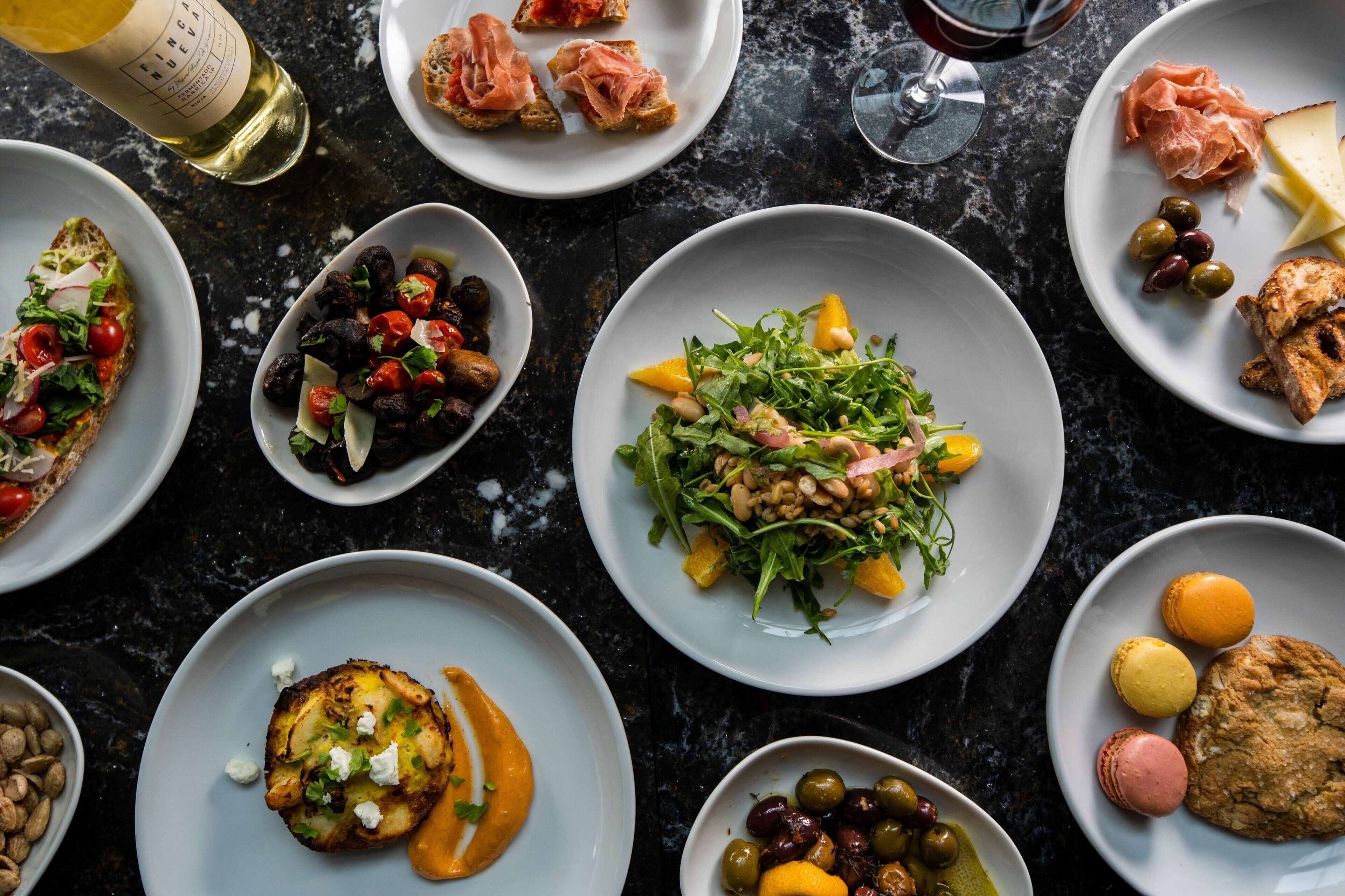 A variety of dishes on plates, including salads, meats, and pastries, arranged on a dark surface.