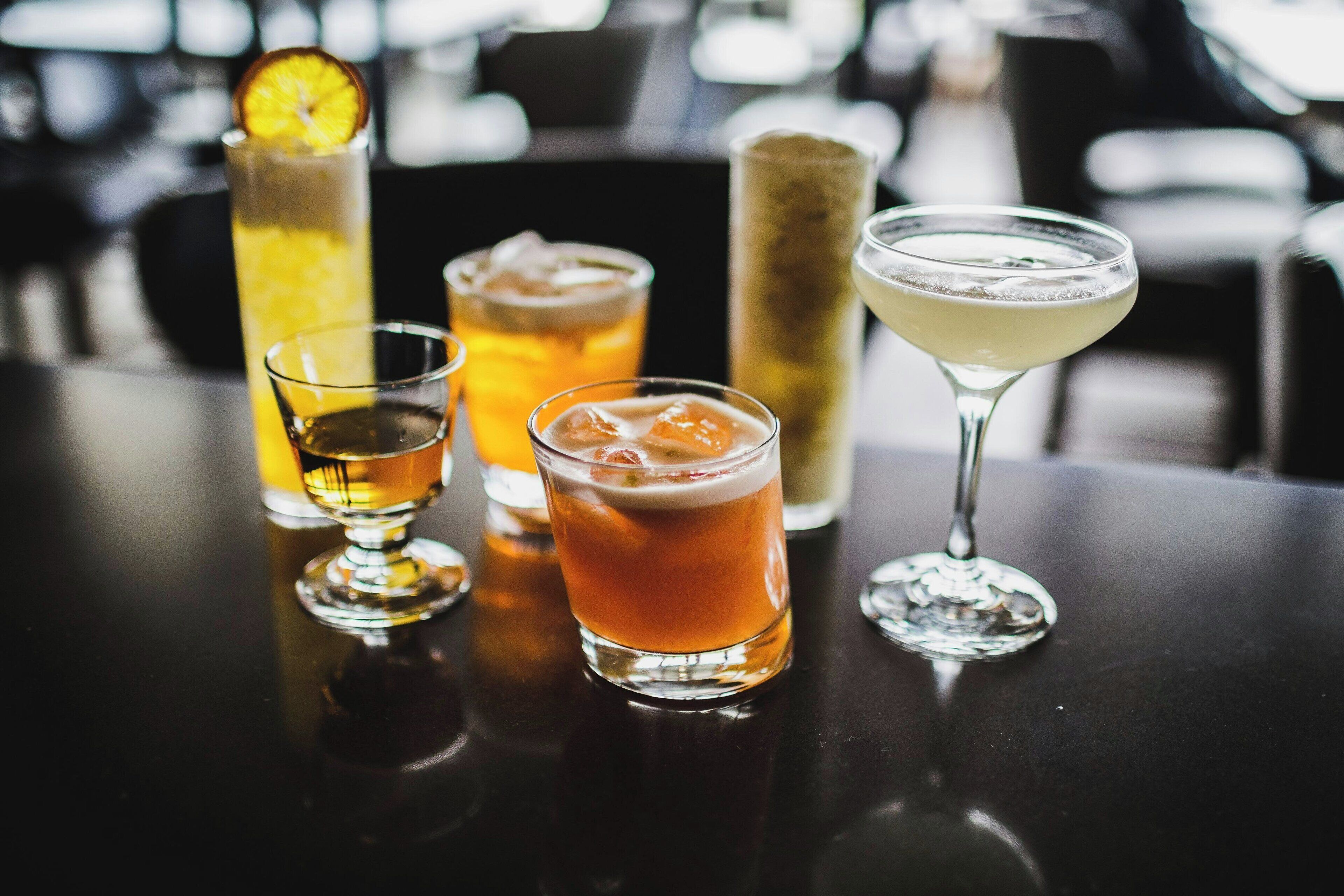 Een barscène met verschillende drankjes, waaronder een hoog glas met een citroenpartje, een laag glas met ijsblokjes en een martini glas.