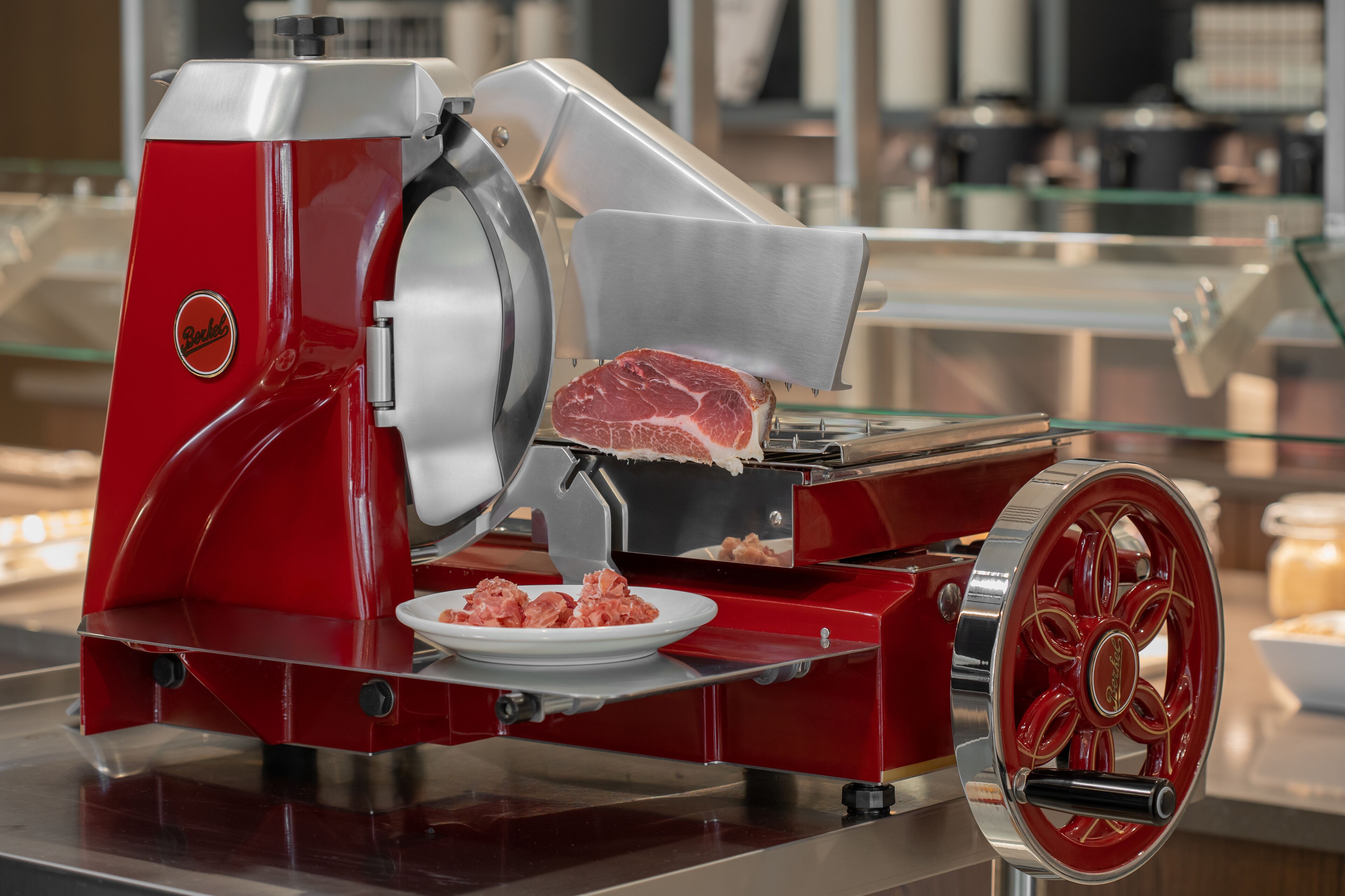 A red meat slicer with a plate of sliced meat and a bowl of raw meat.