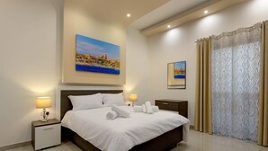 Habitación de hotel con una cama grande, dos mesitas de noche con lámparas, un cabecero y un cuadro de una escena costera.
