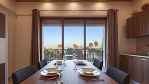 Comedor con una mesa dispuesta para cuatro, ventanas amplias y vistas a palmeras y una grúa.
