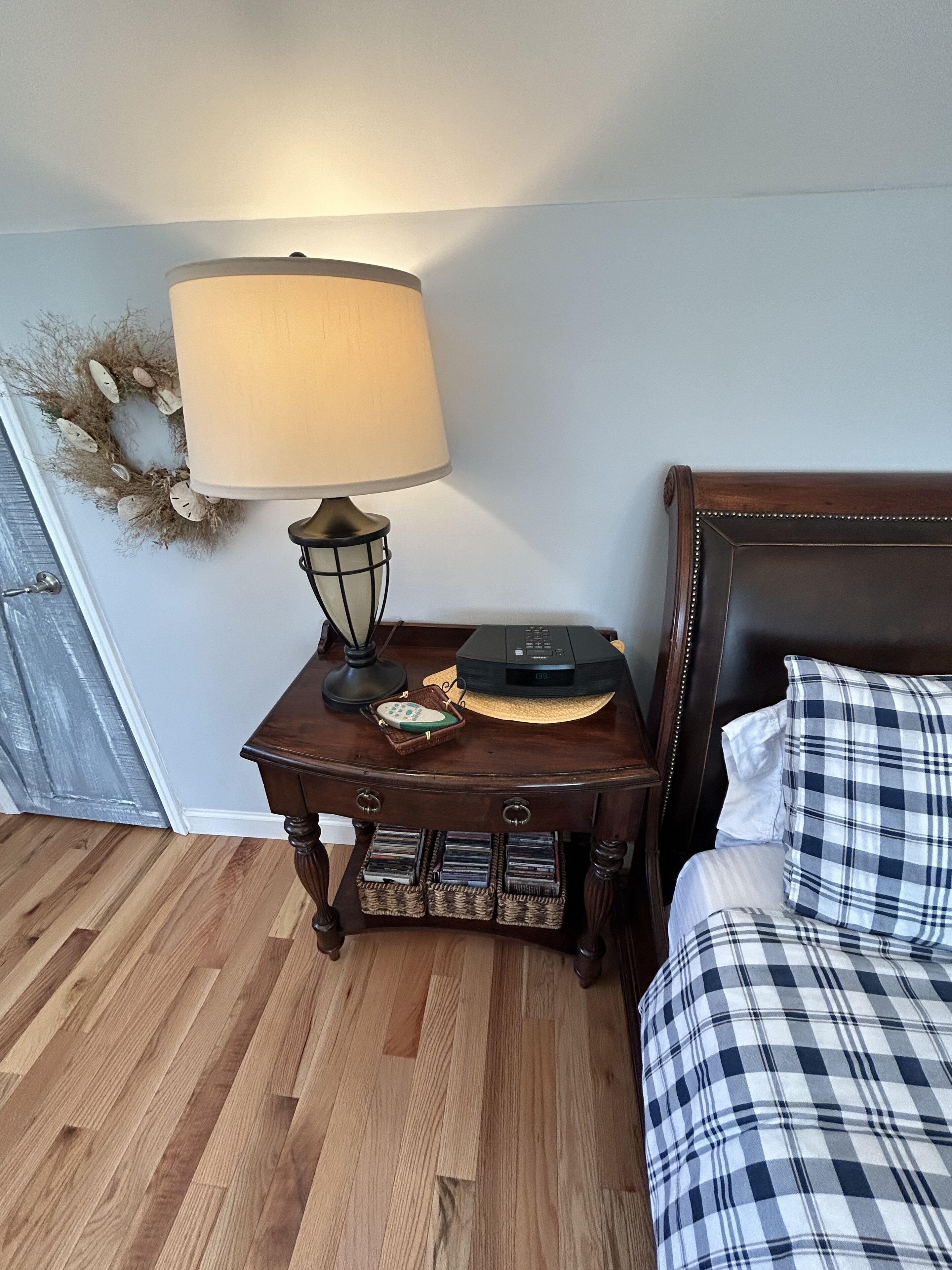 A bedroom with a wooden nightstand, a lamp, a remote control, and a bed with a plaid bedspread.
