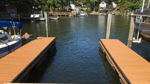 Eine hölzerne Steg ragt in ruhiges Gewässer, im Hintergrund sind Häuser und Boote zu sehen.